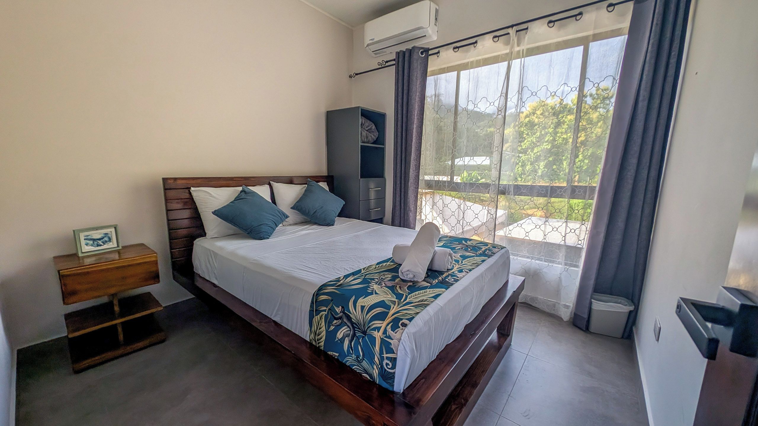 A hotel room with a bed, a nightstand, a wardrobe, and a window with curtains.