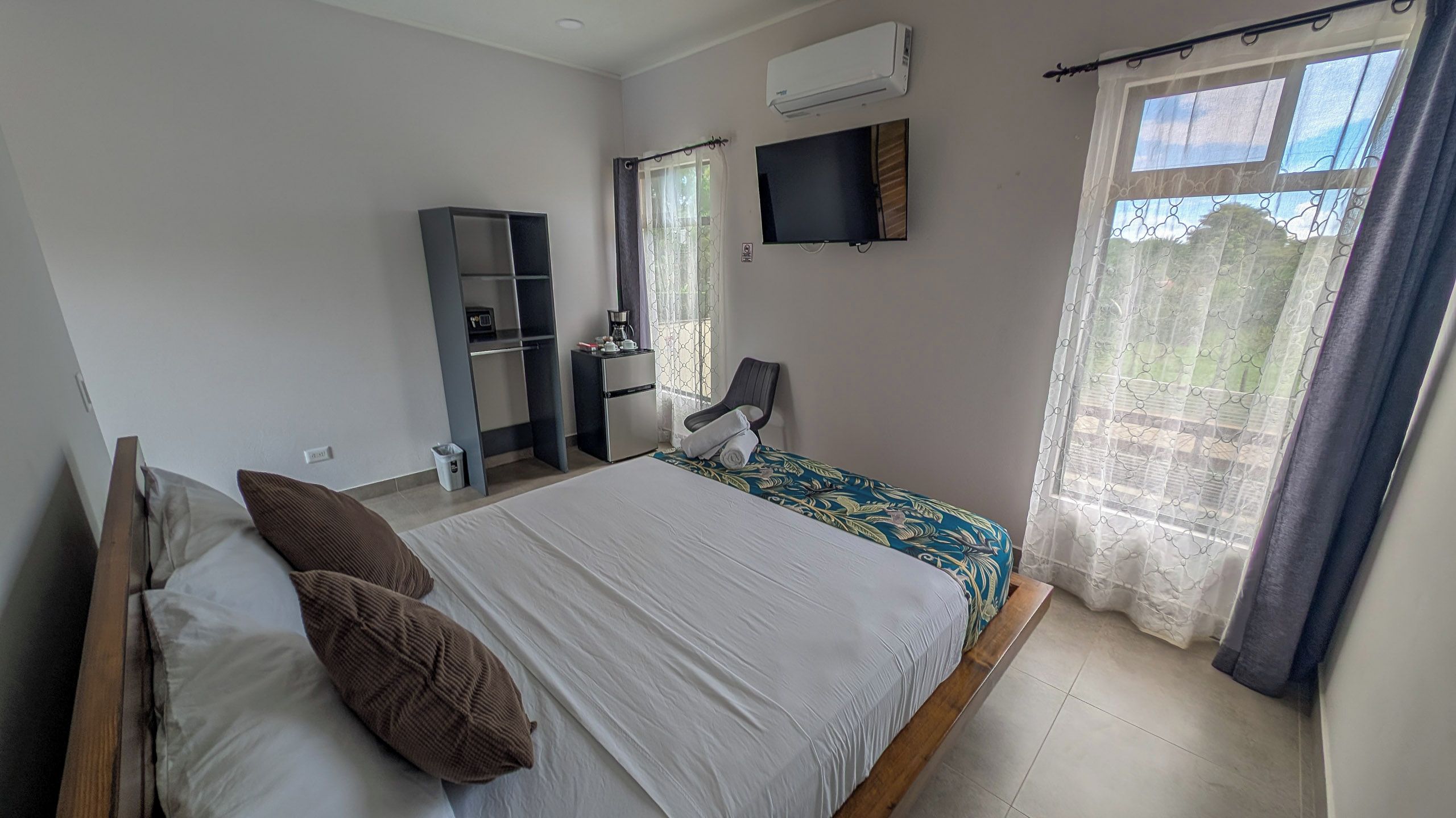 Une chambre à coucher comprenant un lit, un bureau, une chaise, un climatiseur et une fenêtre avec des rideaux.