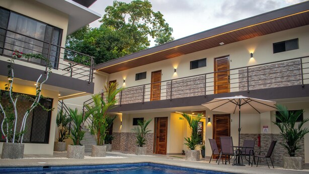 Un hotel moderno con piscina, asientos exteriores y un balcón con vistas a los árboles.