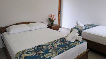Una habitación de hotel con dos camas, cabecera de madera, mesita de noche con un florero y un espejo.