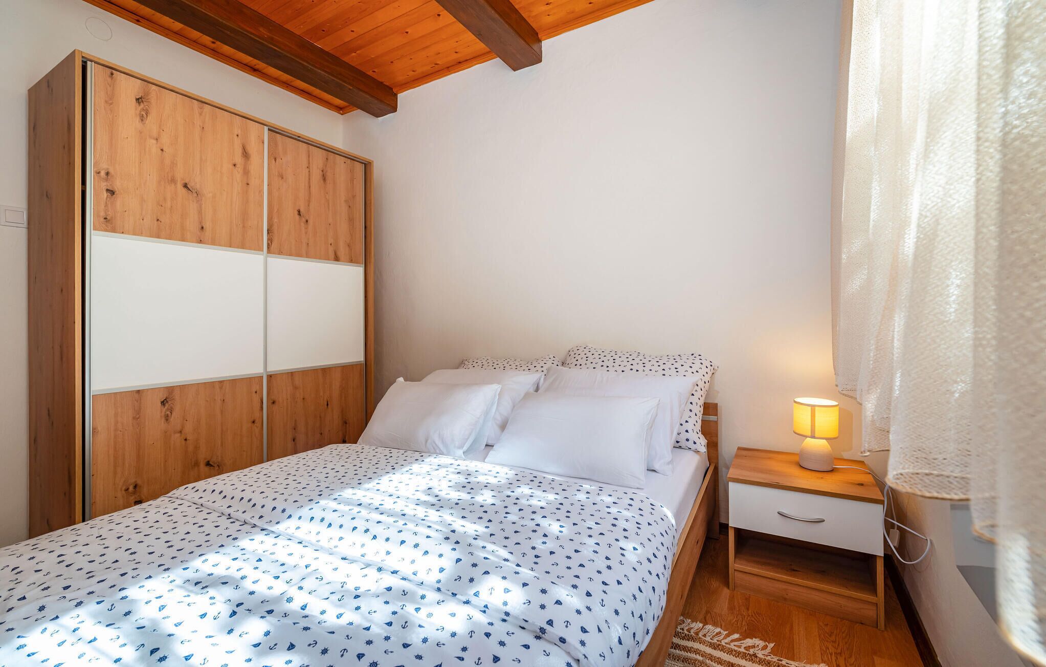 Un dormitorio con cama, mesita de noche, armario de madera y ventana con cortinas.