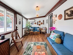 A cozy living room with a blue sofa, wooden flooring, and a large window.