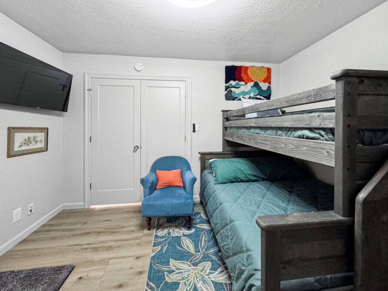 Une chambre avec un lit superposé, une chaise, une porte et un téléviseur fixé au mur.