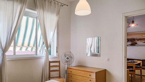 A bedroom with a bed, a wooden dresser, a standing fan, and a window with curtains. - Nice apartment in Giardini Naxos with WiFi (Giardini Naxos)
