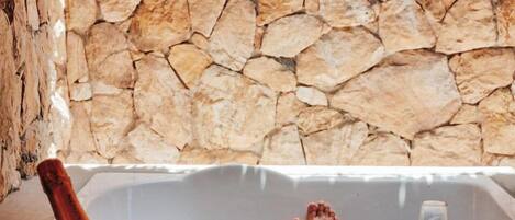 A stone wall, a bathtub, a bucket, and a glass of wine.