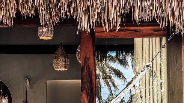 A hammock in a room with a thatched roof, a bed, and a view of a garden. - Pousada Vayú  (Amontada)