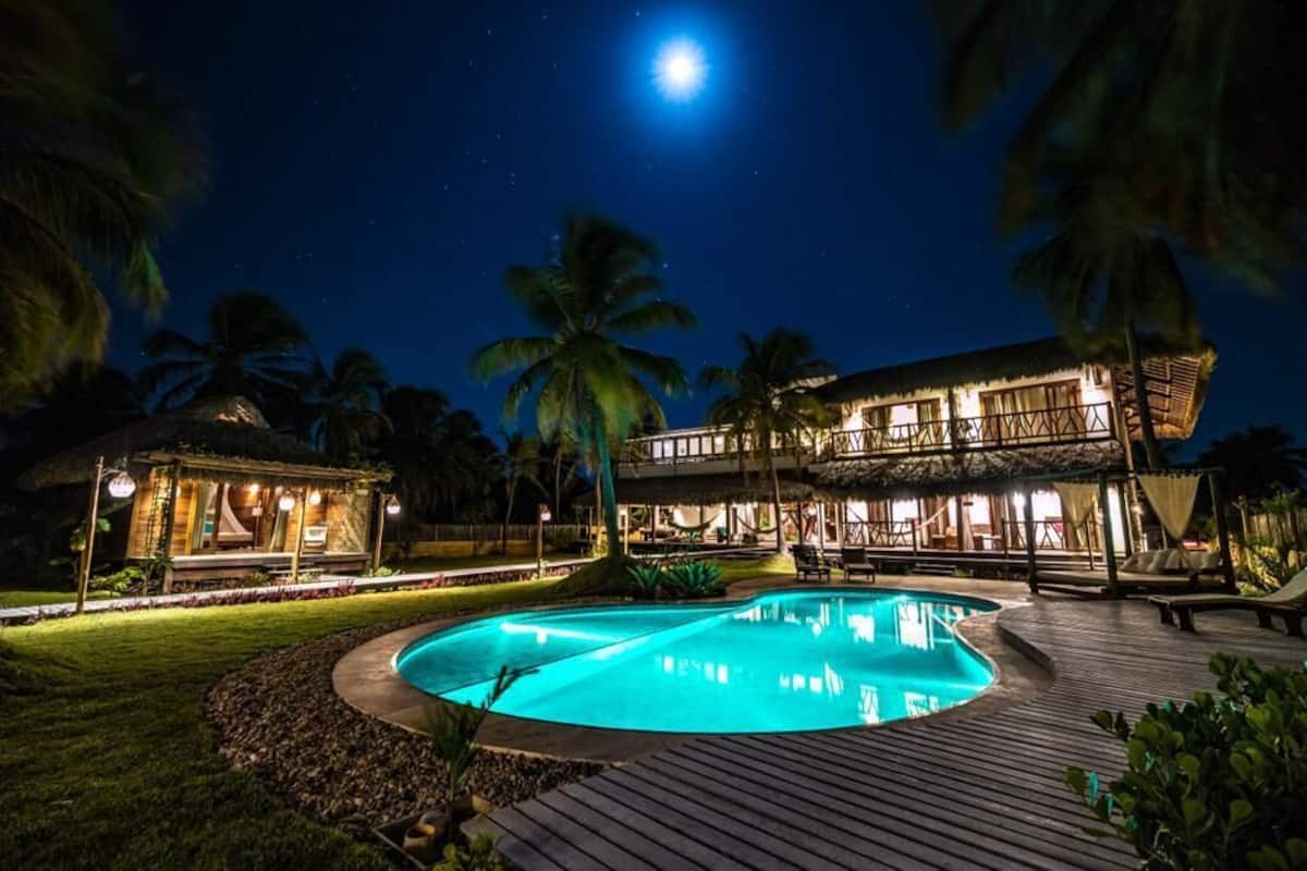 A nighttime view of a resort with a swimming pool, palm trees, and a building with multiple balconies.