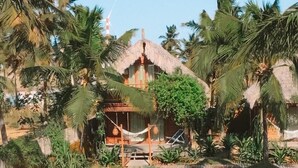 A swimming pool with a person in the water, surrounded by palm trees and a thatched-roof building. - Pousada Vayú  (Amontada)