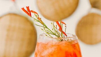 A hand holding a glass with a red drink and a sprig of rosemary.