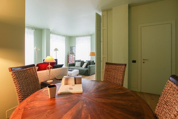 A dining area with a round wooden table, two wicker chairs, and a red cushion.