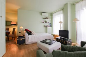 A hotel room with a bed, a television, a desk with a lamp, a suitcase, and a sofa.