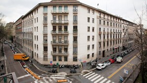 A multi-story building with balconies, a crosswalk, and parked vehicles.