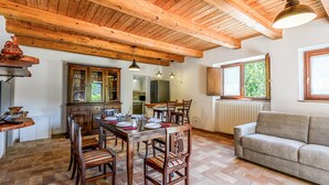 L’intérieur est de style rustique, avec une table à manger en bois, disposée pour accueillir quatre personnes, et entourée de chaises en bois. Un canapé est placé près d’une fenêtre, d’où l’on peut admirer la verdure environnante.