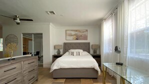A modern bedroom with a large bed, two bedside tables, a dresser, a glass coffee table, and a large window with sheer curtains. - Private Paradise - Large, Peaceful Studio w Patio (Naples)