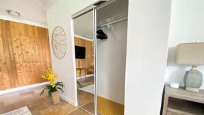 A modern room with a wooden wall, a sliding glass door closet, a potted plant, and a lamp on a bedside table. - Private Paradise - Large, Peaceful Studio w Patio (Naples)