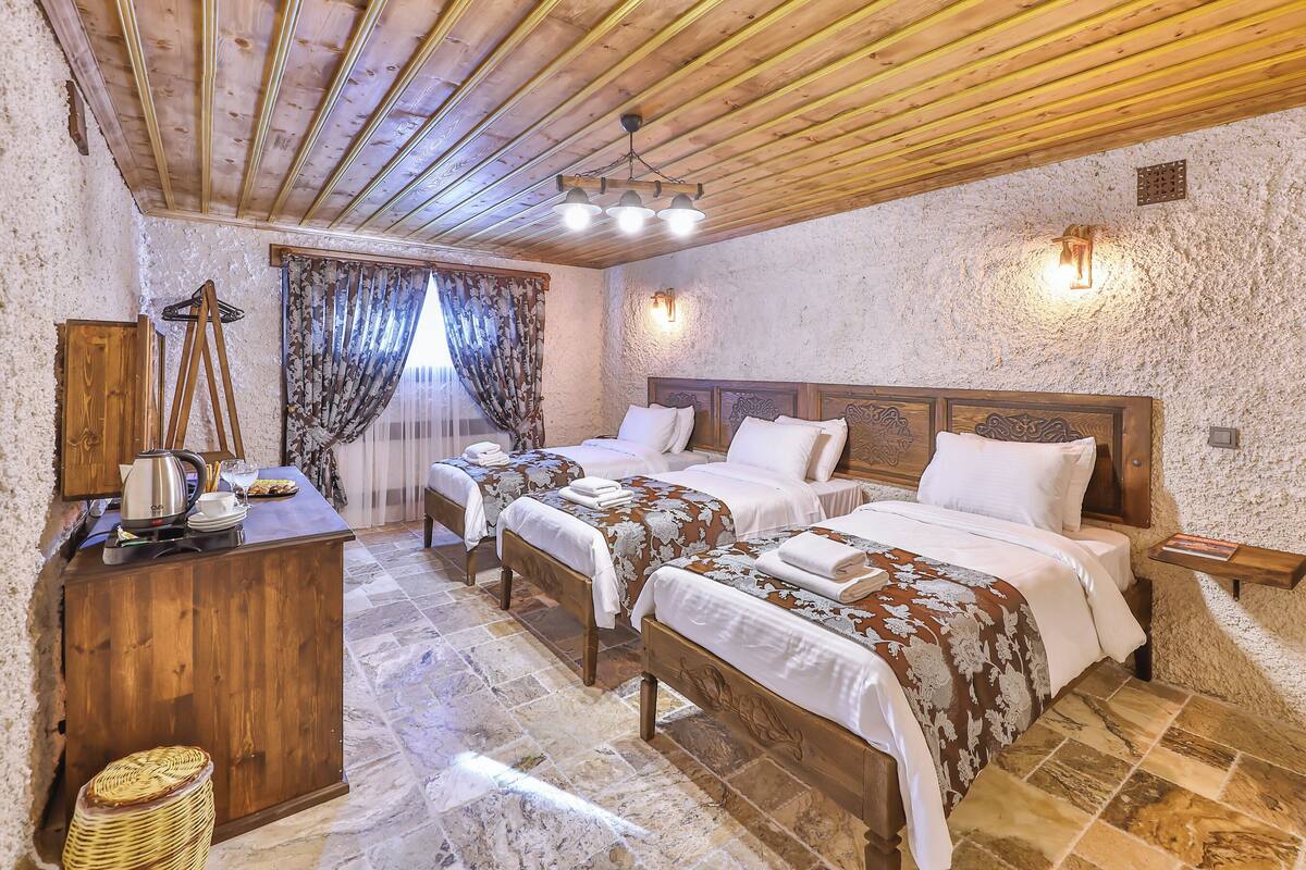 Una habitación con tres camas de madera, un escritorio de madera con una tetera y un suelo de baldosas de piedra.