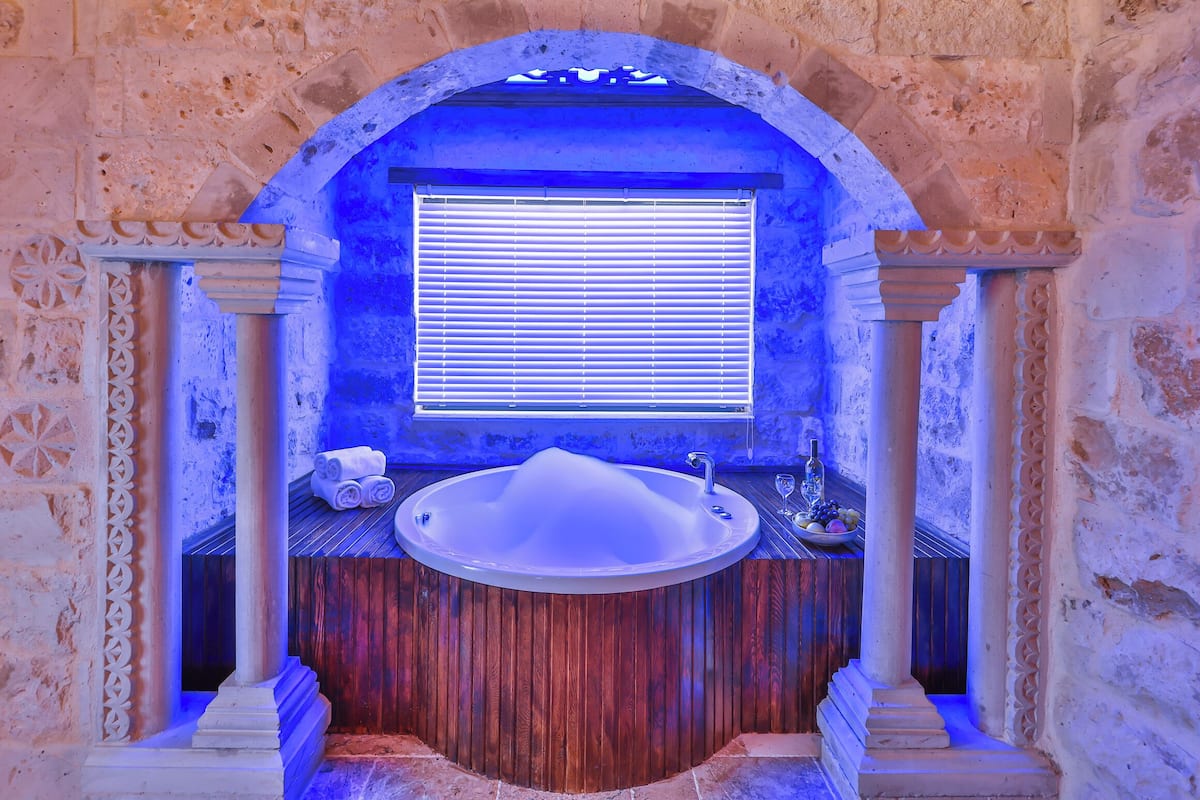 Un baño con una bañera independiente, una ventana con persianas y un adornado en la pared.