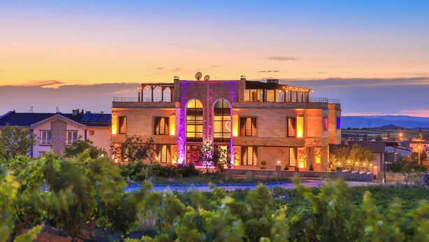 A two-story building with a balcony, large windows, and a view of the surrounding landscape.