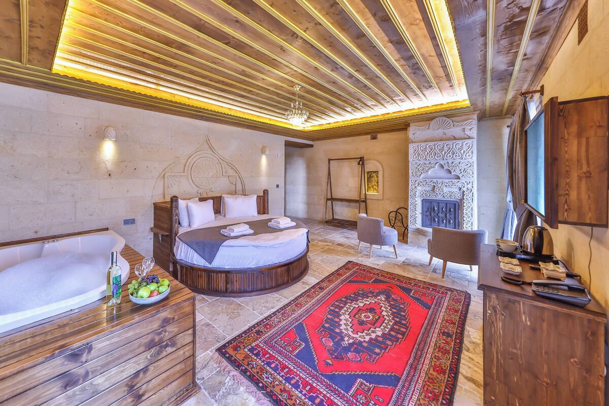Un dormitorio con una cama grande, una bañera, una chimenea y techo de madera.