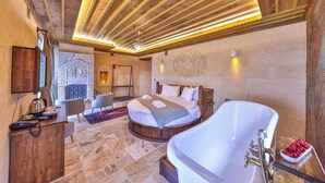 A bedroom with a large white bathtub, a wooden ceiling, and a stone floor.