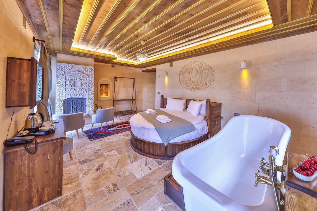 Un dormitorio con una bañera blanca grande, techo de madera y suelo de piedra.