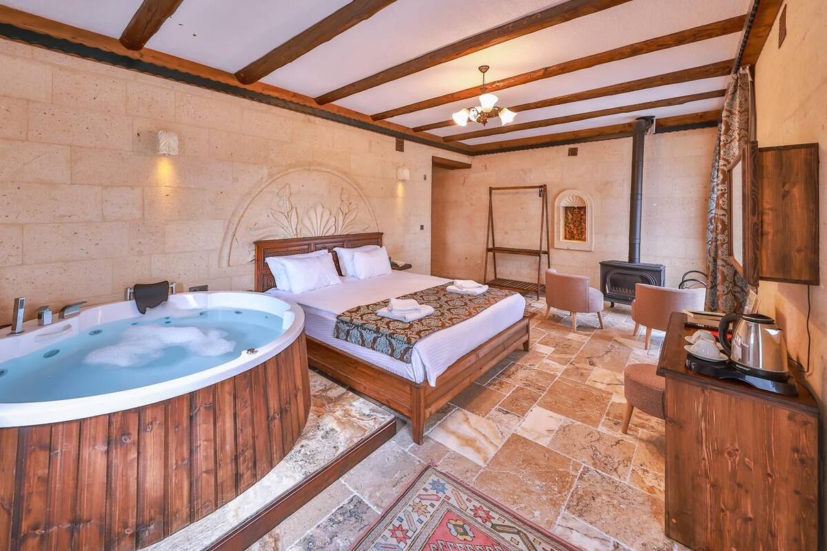 Un dormitorio con una bañera de madera grande, una cama con manta estampada, un escritorio de madera y una chimenea.