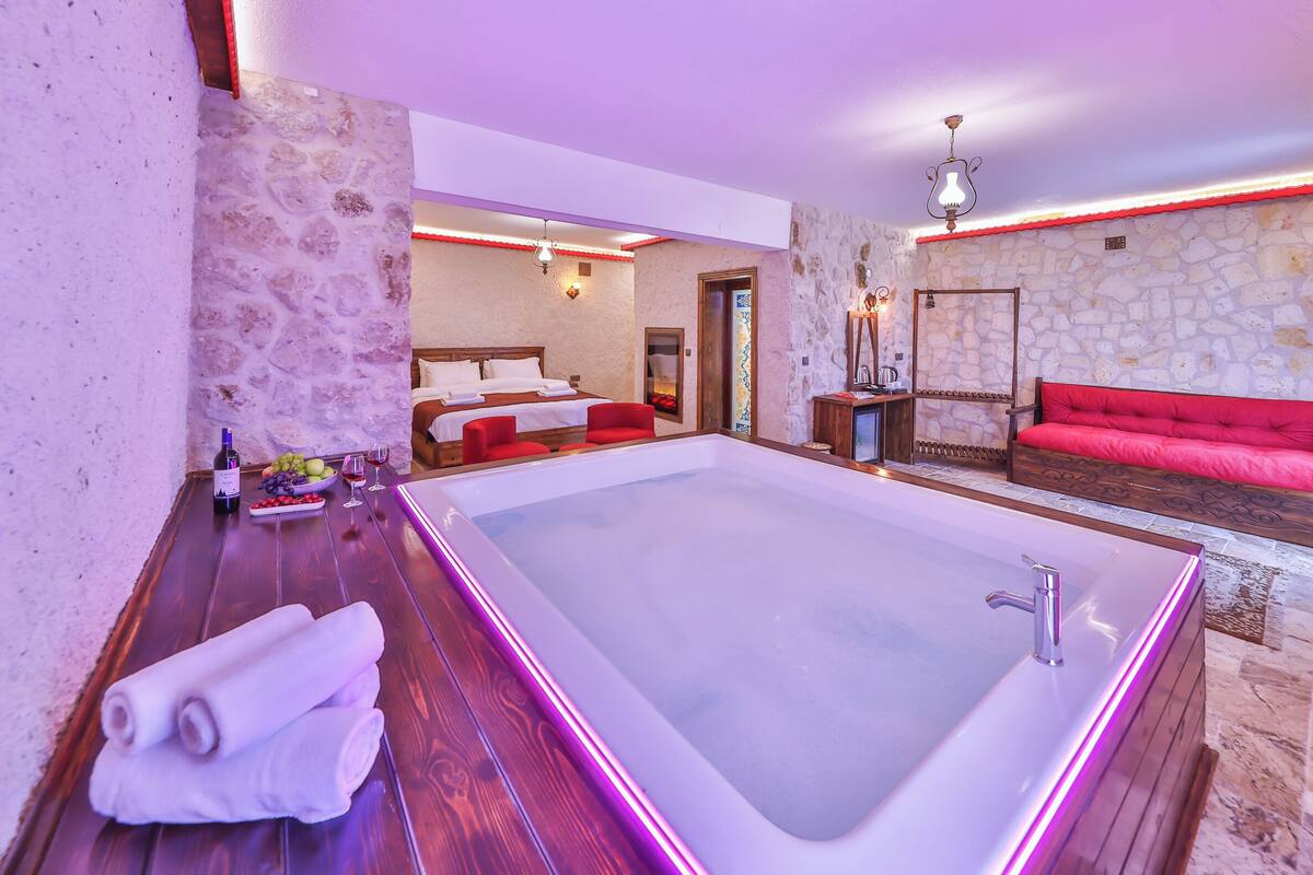 Un cuarto de spa con una bañera grande, un sofá rojo y una mesa de madera con toallas y fruta.