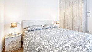 Une chambre à coucher comprenant un lit, deux lampes de chevet, une table de chevet avec des tiroirs et une armoire en bois.
