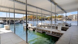 A covered dock area with boats, a bridge in the background, and a waterfront view. - Lakeside Condo! Pool/HotTub! 3 MasterSuites! MC1C (Lake Ozark)