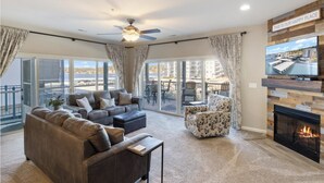 A spacious living room with a fireplace, a ceiling fan, and a large TV. - Lakeside Condo! Pool/HotTub! 3 MasterSuites! MC1C (Lake Ozark)