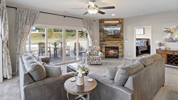 A spacious living room with a fireplace, a ceiling fan, and a large window overlooking a garden. - Lakeside Condo! Pool/HotTub! 3 MasterSuites! MC1C (Lake Ozark)
