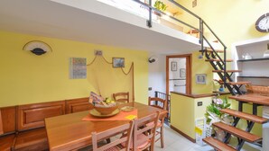 Ein Essbereich mit Holztisch und -stühlen, eine Treppe und eine kleine Küchenzeile mit Kühlschrank.