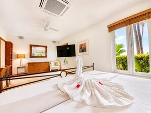 A hotel room with a bed, a television, a wooden dresser, a mirror, and a window with a view of palm trees.