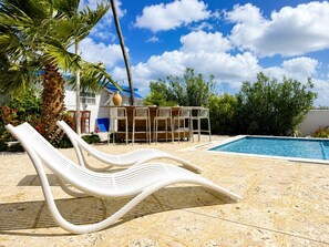 Zona de piscina con sillas de descanso, una piscina y un edificio al fondo.