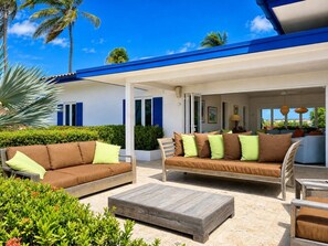 An outdoor seating area with two sofas and a coffee table, surrounded by greenery and palm trees.