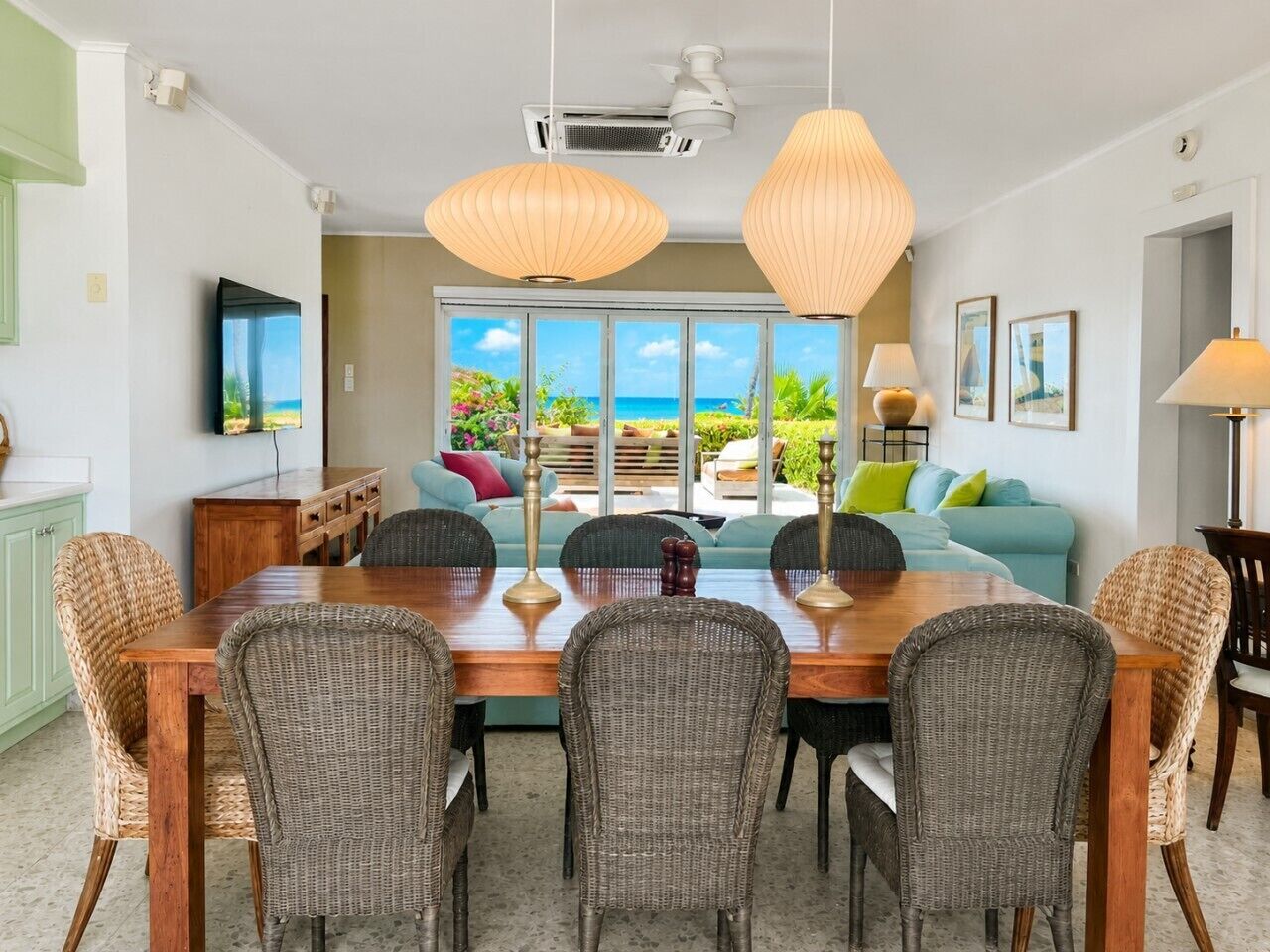 A dining area with a wooden table and wicker chairs, a television, and a view of the outdoors.