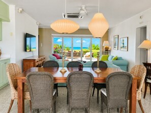 Un comedor con mesa de madera, sillas de mimbre, televisor y vistas al exterior.