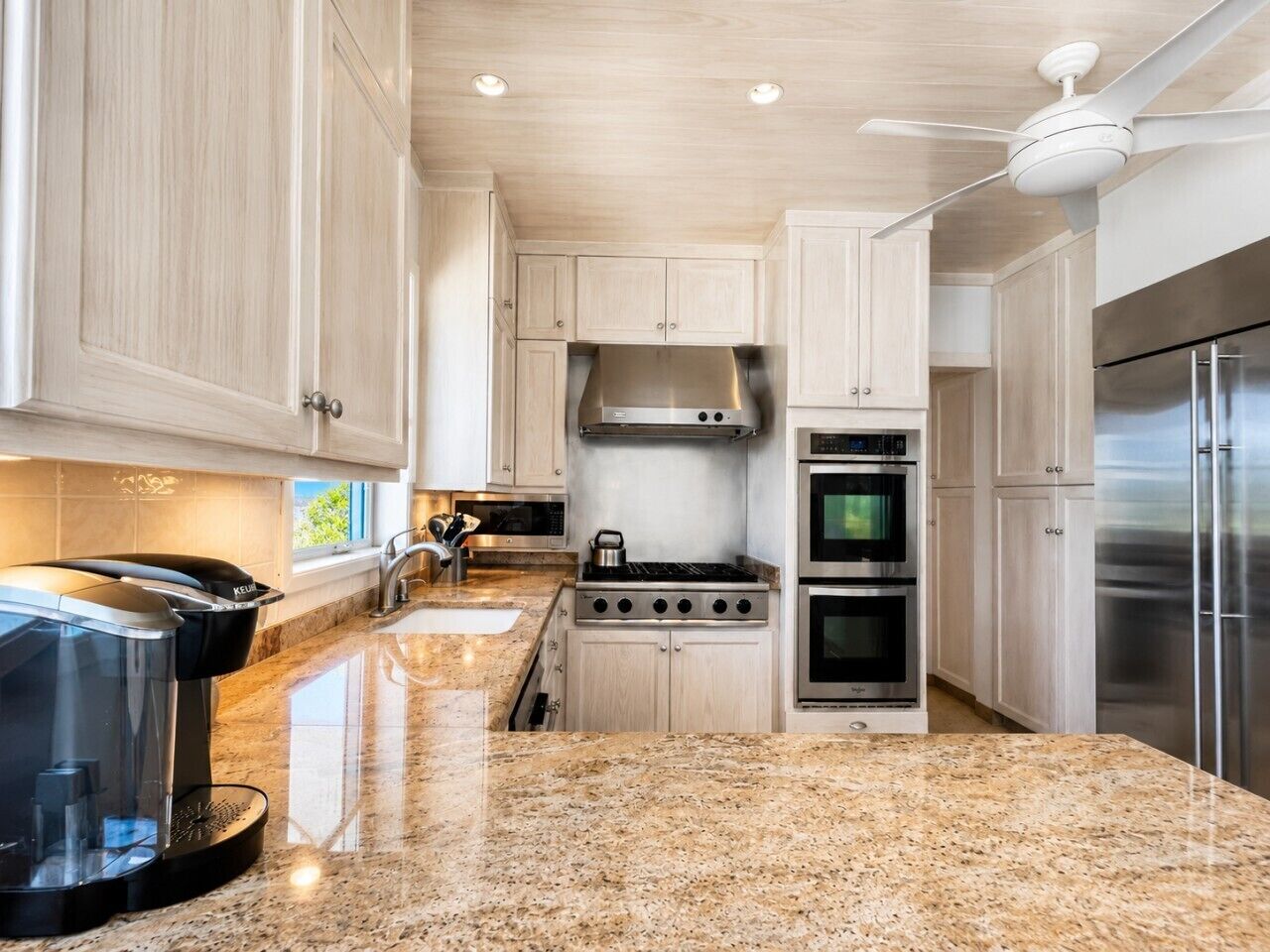 A modern kitchen with granite countertops, stainless steel appliances, and light wood cabinetry.