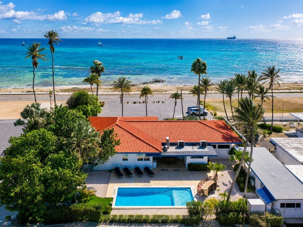 Une propriété située en bord de mer, dotée d’une piscine, de palmiers et offrant une vue sur l’océan.