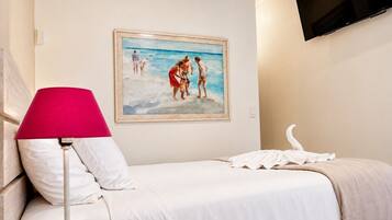 Een hotelkamer met een bed, een schilderij van een strand, een televisie en een rode lamp.