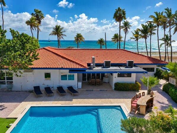 A beachfront property with a swimming pool, lounge chairs, and a patio area.