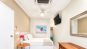 Une chambre d’hôtel avec un lit, une table de chevet, une lampe, une commode, une télévision et une œuvre d’art au mur.