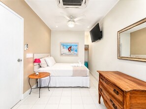 Habitación de hotel con cama, mesita de noche, lámpara, cómoda, televisión y una obra de arte en la pared.