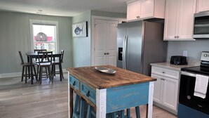 A kitchen with a wooden island, stainless steel appliances, and a dining area with chairs and a table.