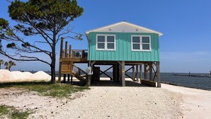 A turquoise beach house with a wooden deck and a staircase leading to a balcony.