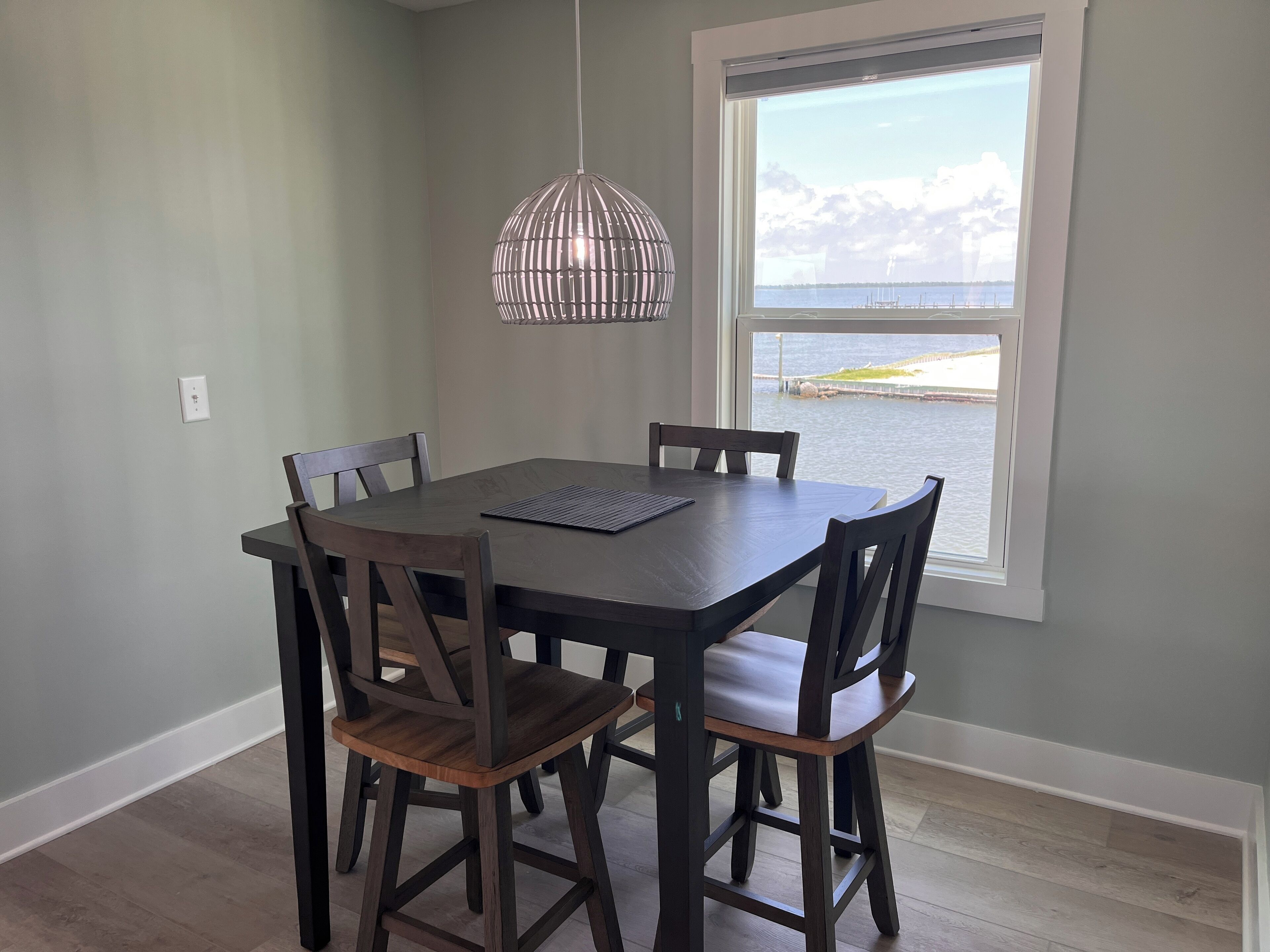 A dining area with a table and chairs, a hanging light fixture, and a window with a view of the water.