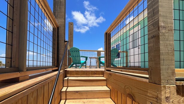 A wooden staircase leading to a deck with a view of the ocean.