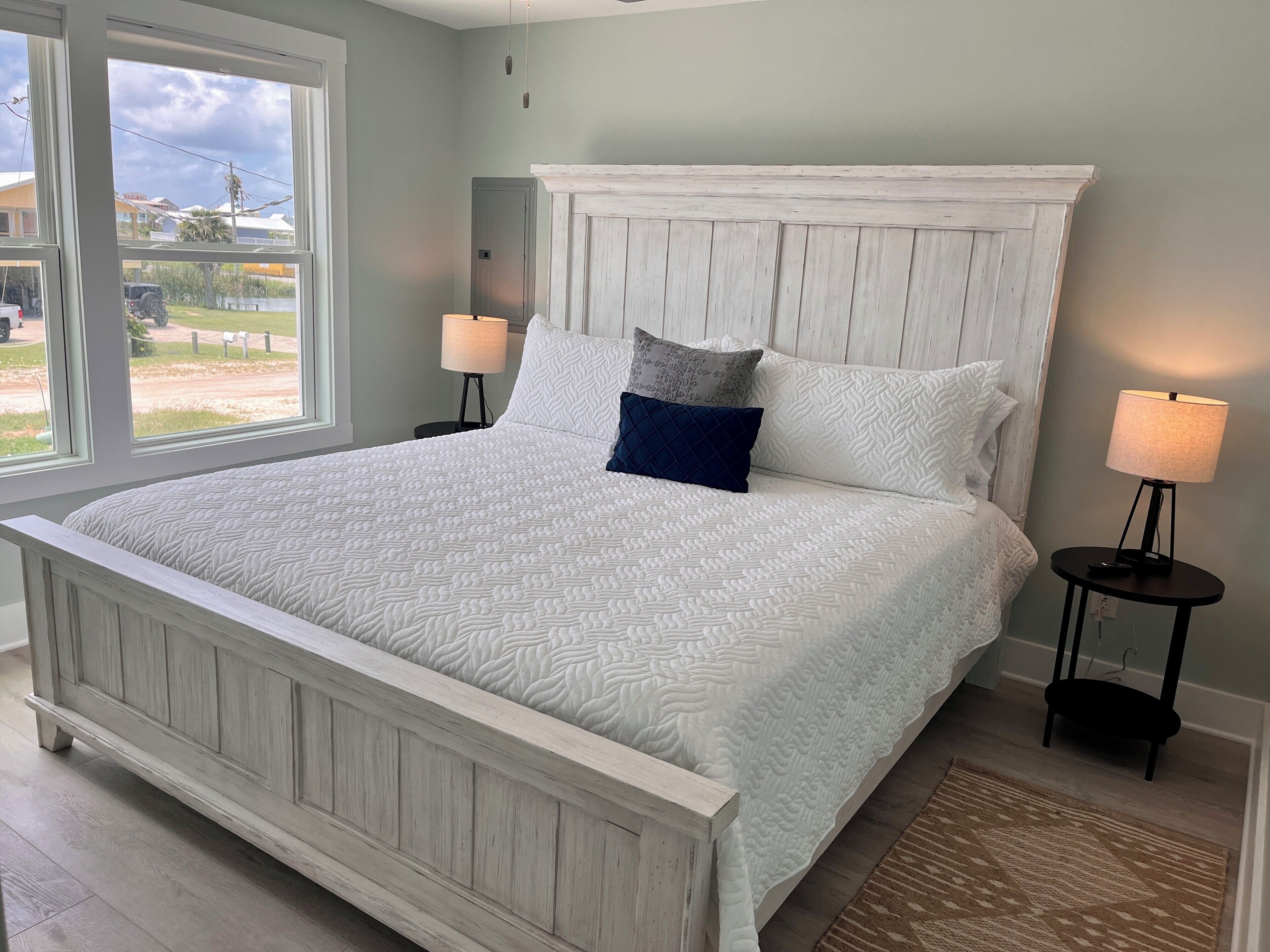 A large bed with a white headboard and footboard, two bedside lamps, and a view of the outdoors through a window.