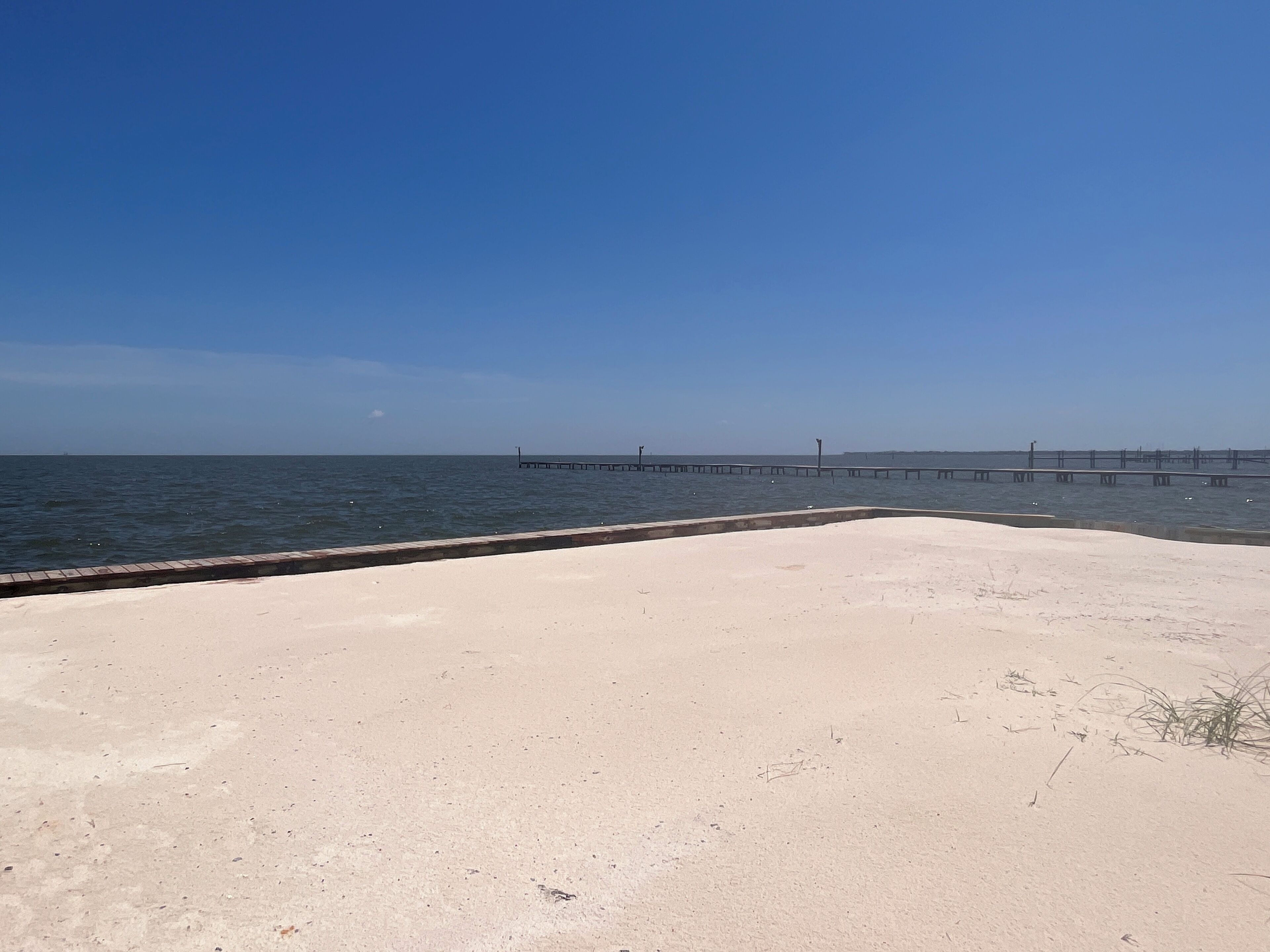 A sandy beach with a long pier extending into the water.