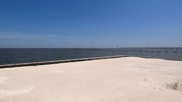 A sandy beach with a long pier extending into the water.